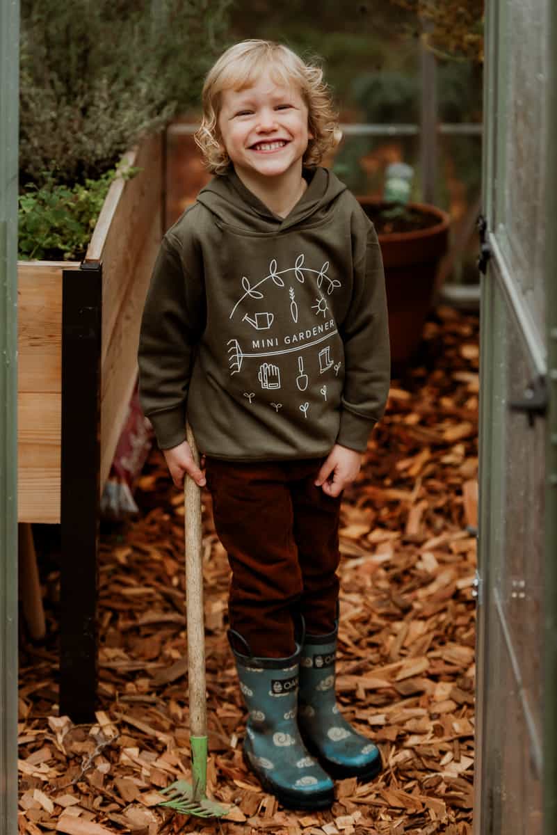 Gardening guide for parents - Child holding child-sized rake inside greenhouse.