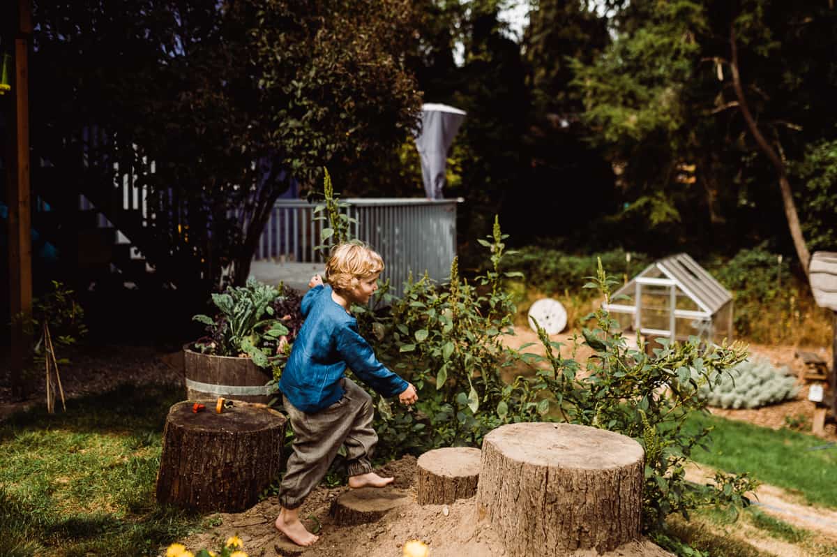 Child hopping on tree trunks in backyard garden.