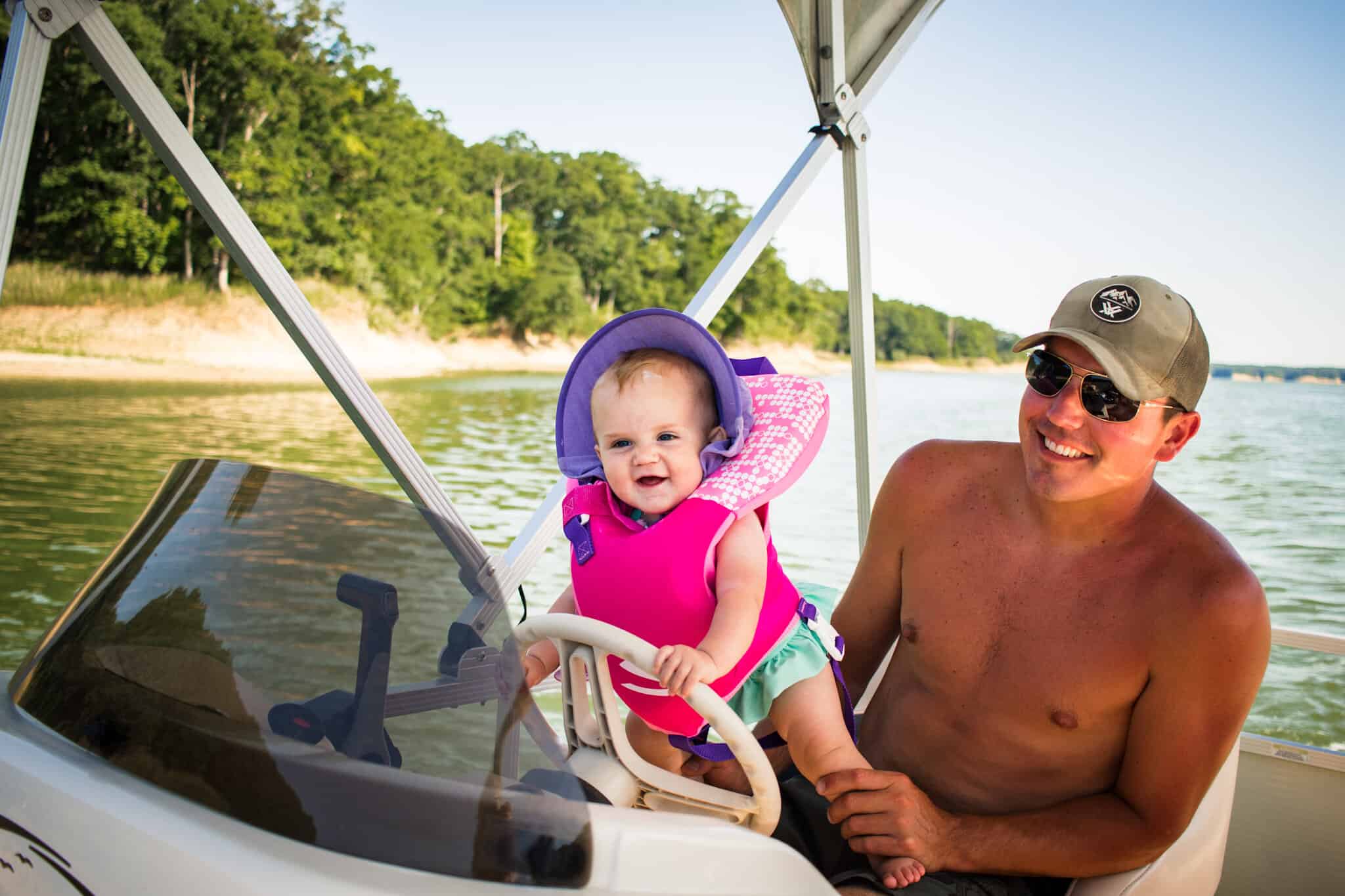 Baby in pink life jacket holding onto boat steering wheel - best life jackets for babies