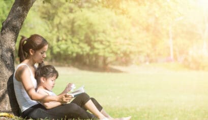 Mother and child read outdoors under a tree