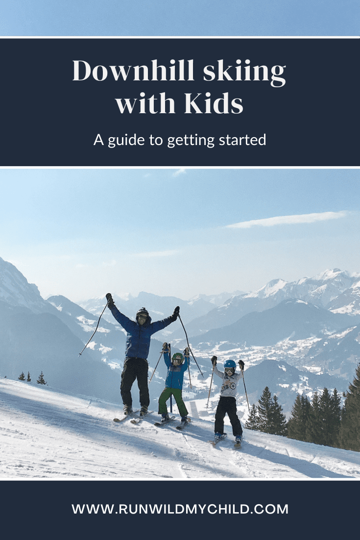 Two young children raising their hands in joy after downhill skiing on a mountain with a parent