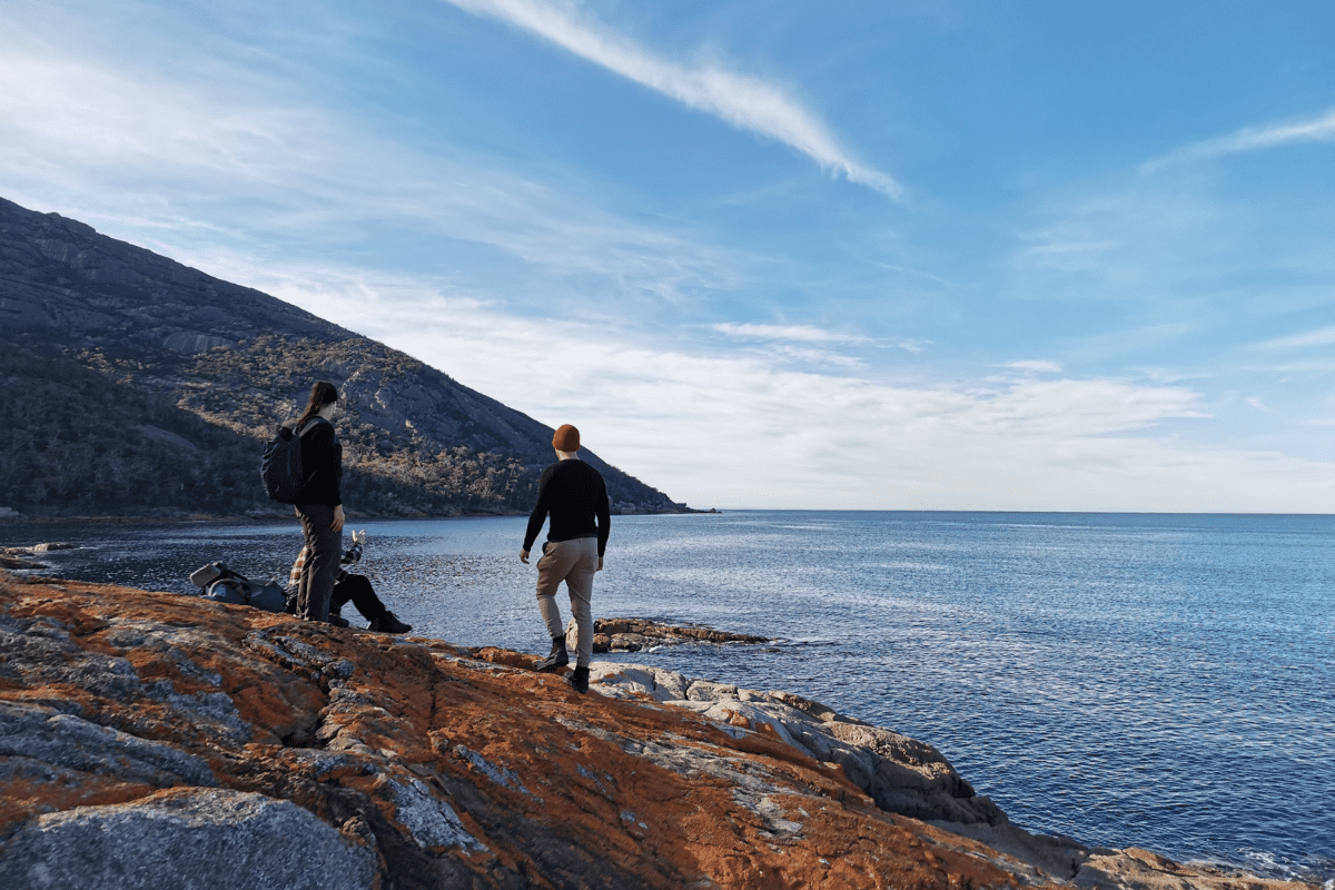 Hiking friends resting on red rock coastline. 