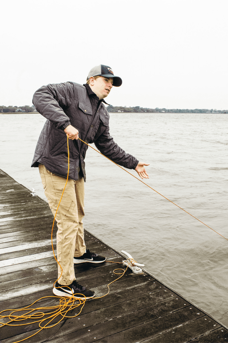 teen boy standing on a dock pulling on a rope line to bring in a crab basket