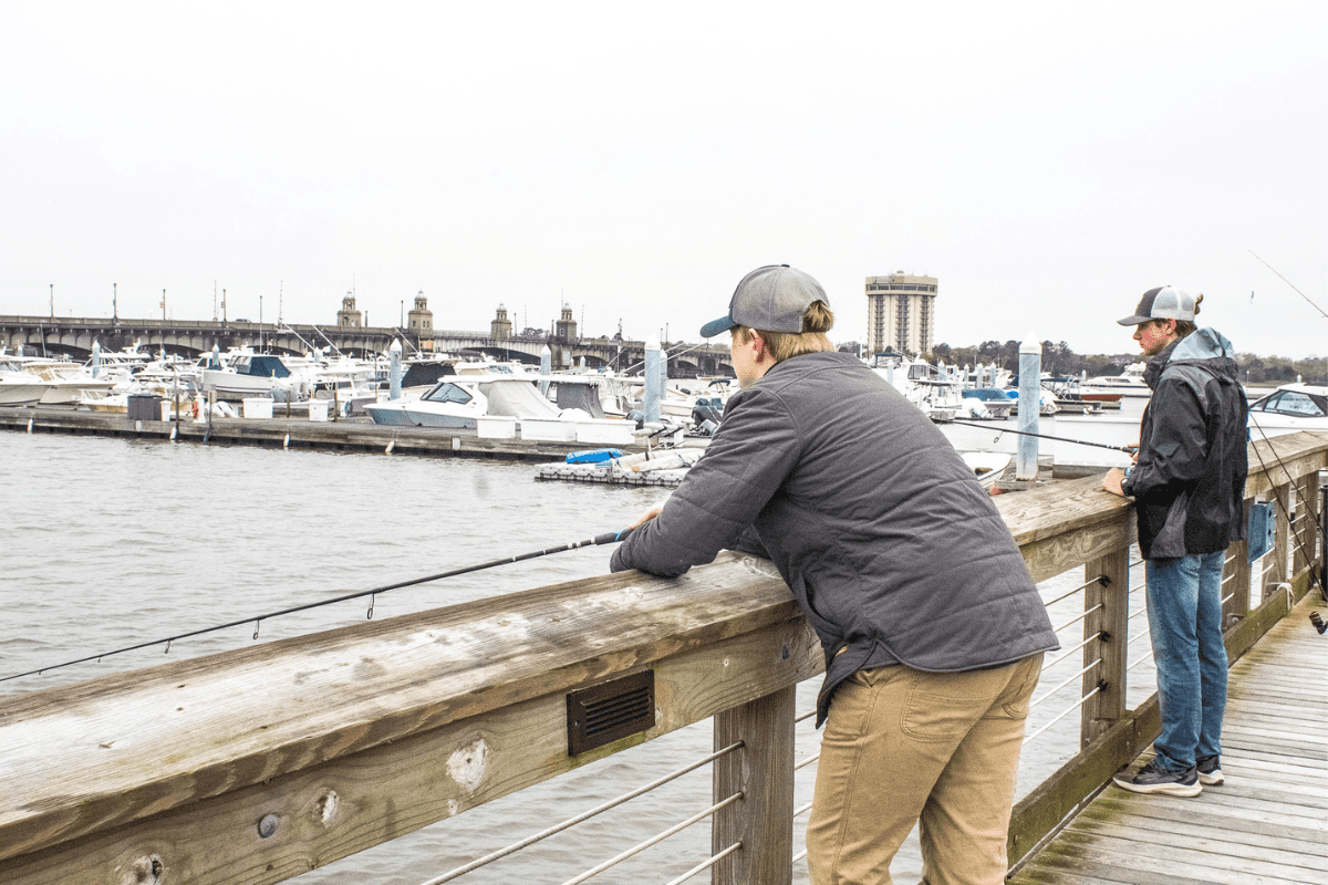 two teen boys standing on a dock with fishing poles trying to catch some live bait for the crab baskets