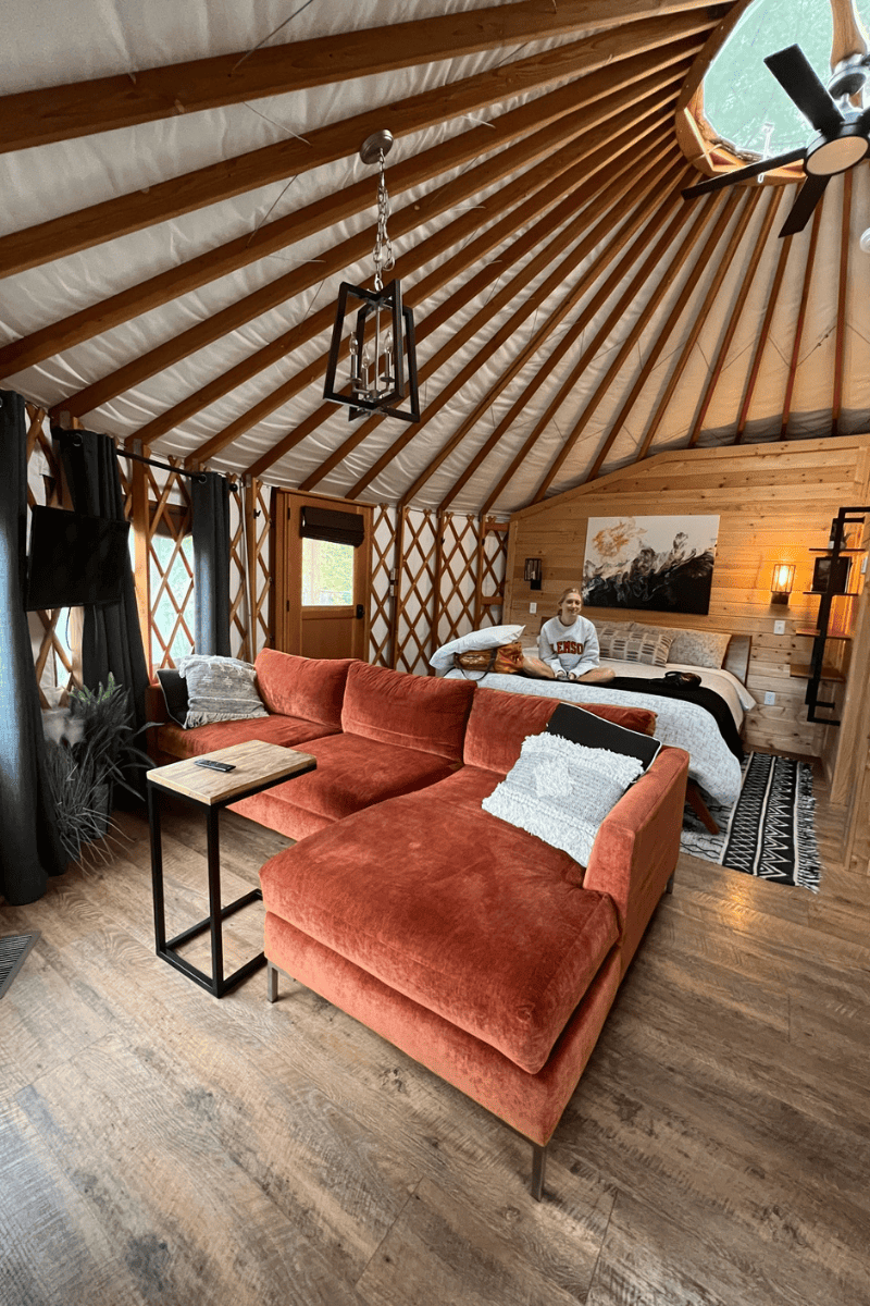 interior of a luxury yurt showing an orange couch, bed, and visible yurt beams on the ceiling above