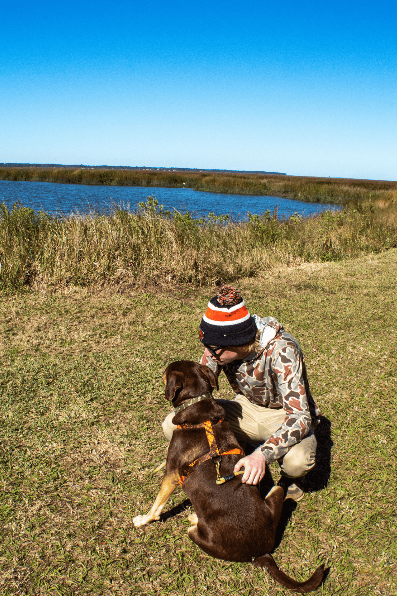 teen boy crouching down with dog next to a lake