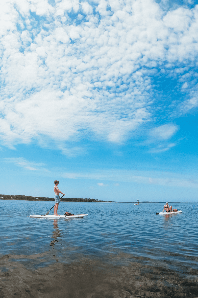 Teens boys on an SUP and a teen girl sitting on an SUP in Gulf County Florida